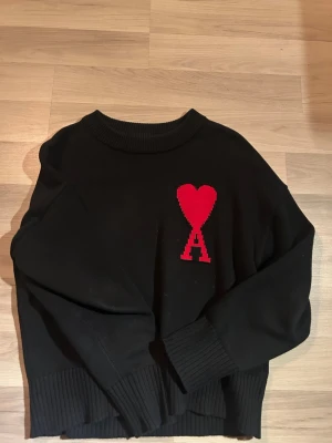 Ami  - En svart Ami Paris tröja som jag säljer då den blivit för liten. Den är använd relativt mycket men det finns inga tydliga tecken på användning 