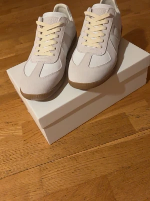 Maison Margiela vita sneakers i mocka - Maison Margiela sneakers i vitt med beige detaljer och gummisula. De är i storlek 43 och i nytt skick. Tveka inte med att höra av dig angående minsta lilla fundering🙏😌