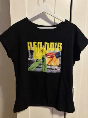 Svart t-shirt med färgglatt tryck - Svart t-shirt med ett stort färgglatt tryck framtill som visar personer i streetstyle och text i gult. T-shirten har rund hals, korta ärmar. Storlek står inte men skulle säga S/M