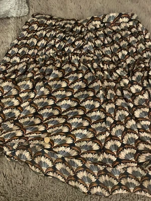 Blommig kortkjol från Harper & Yve - Supersnygg kortkjol från Harper & Yve i storlek XS. Kjolen har ett blommigt mönster i beige, brun, svart och vit med elastisk midja och knappdetalj framtill. Perfekt för dig som vill ha en unik och färgglad kjol med skön passform.