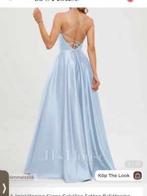 Ljusblå långklänning i satin - Säljer en elegant ljusblå långklänning från JJ's House i glansig satin. Klänningen har smala axelband som korsas i ryggen och snörning baktill. Den har en figurnära överdel och ett svepande, utsvängt kjolparti. Perfekt för bal eller student!