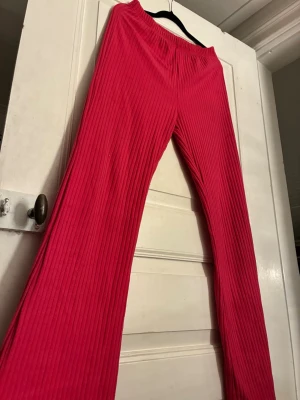 Ribbstickade rosa mjukisbyxor från Shein  - Säljer ett par ribbstickade mjukisbyxor från Shein i stark rosa färg. Byxorna har elastisk midja och raka ben med en loose passform. Materialet är mjukt och stretchigt, perfekt för chill dagar. Inga fickor eller synliga detaljer förutom ribbningen.