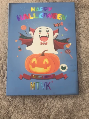 MTVK Happy Halloween ögonskuggspalett - Stor ögonskuggspalett med Halloween-tema från MTVK. Paletten innehåller massor av färgstarka och neutrala nyanser i både matta, skimriga och glittriga finishes. Färgerna sträcker sig från orange, lila, blå, grön, guld, brun till rosa och silver. Perfekt för kreativa och färgglada looks.