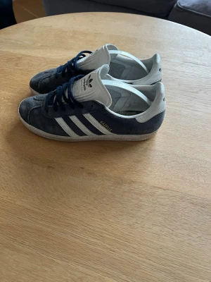 Adidas Gazelle  - Säljer ett par klassiska Adidas Gazelle sneakers i mörkblå mocka med vita detaljer och snörning. Priset kan diskuteras vid en snabb affär skorna är använda men finns mycket kvar i dom hör av vid minsta lilla fråga!