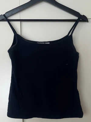 Mörkblå linnetopp från Gina Tricot - En enkel och stilren mörkblå linnetopp från Gina Tricot med smala axelband. Toppen är rak i modellen och gjord i mjuk bomull, perfekt till sommaren eller som basplagg. Passar till allt och är lätt att styla med andra plagg.