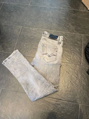 Replay ljusgrå  jeans - Säljer ett par ljusgrå Replay jeans. Jeansen har slitna detaljer framtill, klassiska fem fickor och svart patch bak i midjan. Snyggt tvättad denim med broderade bakfickor och smal siluett. Perfekta till sneakers och hoodie.