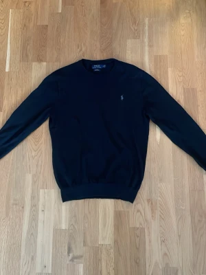Svart tröja Polo Ralph Lauren M - Klassisk svart tröja från Polo Ralph Lauren i slim fit-modell. Tillverkad i mjuk pima bomull och har rund hals samt diskret logga broderad på bröstet. Perfekt till jeans eller chinos för en clean look.