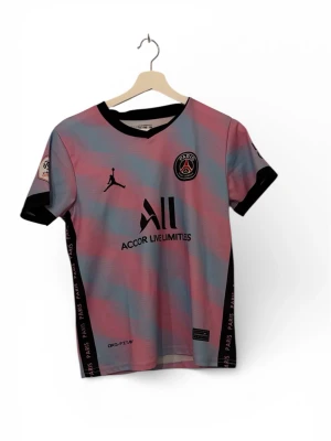PSG Jordan Matchtröja – Pastellrosa/Ljusblå (Unisex) -  Snygg Paris Saint-Germain-tröja i unikt pastellmönster med rosa och blå nyanser. Svarta detaljer vid krage och ärmslut, Jordan-logga på bröstet samt “ALL – Accor Live Limitless” som sponsortryck. Officiellt Ligue 1-märke på ärmen och “PARIS”-band längs sidorna. Tillverkad i Dri-Fit funktionsmaterial – lätt, bekväm och andas bra. Tar emot bud. Den har krympt till st 158  ✔ Bra skick / knappt använd ✔ Passar både träning och streetwear