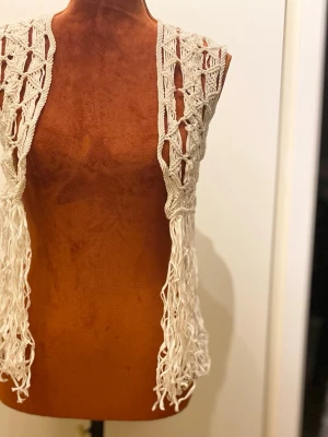 Vit virkad väst med fransar H&M Divided S/M - Ärmlös väst med fransar nedtill. Virkad design. Liten i storlek 45% viskos Längd: 58 cm Bystvidd: 41 cm  Inga bilder när den sitter på mig! Katter finns i hemmet!