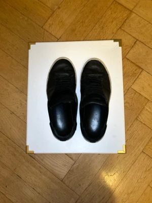 Axel Arigato sneakers i svart skinn med vit sula - Säljer ett par svarta sneakers i skinn med klassisk vit sula och svarta skosnören. Skorna har rund tå och platt sula, perfekt för en clean och stilren look. Passar till det mesta och är riktigt enkelt att matcha med olika outfits.