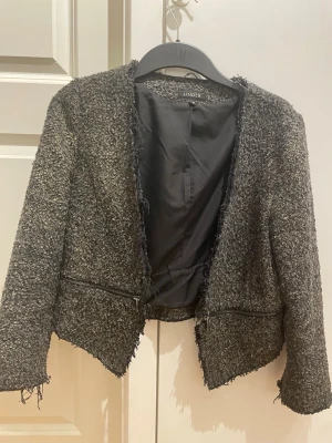 Svart bouclé kavaj från Lindex - Säljer en svart bouclé kavaj från Lindex i storlek 40. Jackan har råa kanter, dragkedjedetaljer framtill och är helfodrad. Perfekt för dig som gillar en lite edgy och trendig look. Passa mig som är 15 år gammal 