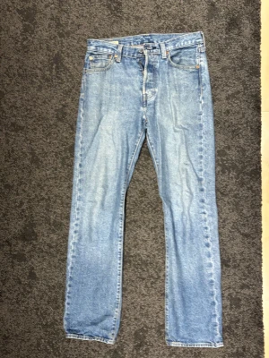 Levi's 501 ljusblå jeans straight fit - Klassiska Levi's 501 jeans i ljusblå tvätt med raka ben och normal passform. Jeansen är tillverkade i slitstarkt bomullsjeans och har fem fickor, knappgylf och Levi's Premium-märke. Perfekta för en avslappnad och tidlös stil.