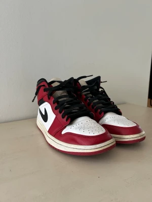 Nike Air Jordan 1 Chicago Mid - Säljer ett par Nike Air Jordan 1 Chicago Mid med klassisk färgblockning i rött, vitt och svart. Skorna är i mycket bra skick med endast tecken på normal användning. Skobox medkommer med en mindre igentejpad spricka.