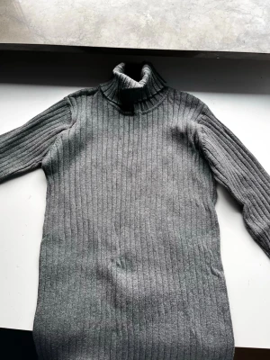 Grå ribbad polotröja från Lindex - Säljer en grå ribbad polotröja från Lindex i storlek M. Tröjan har lång ärm, hög polokrage och är gjord i mjukt stickat material. Perfekt för kyliga dagar och enkel att styla med jeans eller kjol.