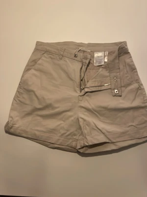 Beige shorts med dragkedja - Säljer ett par klassiska beige shorts från HM med midwaist passform. De har praktiska fickor på sidorna, bälteshällor och stängs med dragkedja och knapp. Perfekta för varma dagar och har en stilren look som funkar till många outfits.