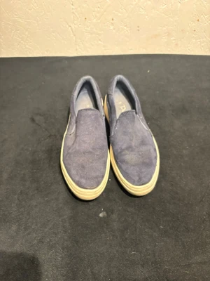 Mörkblå slip-on sneakers - Säljer ett par mörkblå slip-on sneakers från Duffy med vit platt sula. Skorna har en enkel och stilren design utan snörning, och är gjorda i mocka med elastiska paneler på sidorna för enkel påtagning. Perfekta för dig som gillar avslappnad stil.