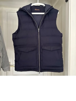 Svart dunväst med huva från Stenströms - Säljer en mörkblå väst från Stenströms med huva och två stora fickor framtill.  Västen är i topp skick och har mycket kvar att ge. Västen är storlek M. Skriv gärna vid funderingar. 