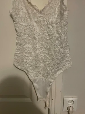 Vit spetsig korsettopp från Amisu - Säljer en vit korsettopp från Amisu i storlek S. Toppen har tunna justerbara axelband och är täckt av snygg spets med vågig kant upptill. Materialet är mjukt och följsamt, perfekt för att skapa en chic look. Passformen är slim och toppen är ärmlös.