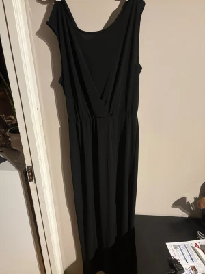 Svart långklänning från Vila - En svart långklänning från Vila med omlott-detalj upptill och ärmlös design. Klänningen har en mjuk och följsam känsla, troligtvis i polyester, och markerad midja. Perfekt för dig som gillar stilrena och enkla plagg med snygg passform.