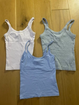 3-pack linnetoppar i pastellfärger - Tre enkla och snygga linnetoppar i ljusrosa, ljusblått och ljusgrått. Alla har smala axelband och är tillverkade i mjuk bomull, perfekta för varma dagar eller som lager under andra plagg.