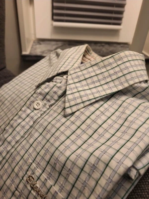 Rutig skjorta från Blend of America, storlek L - Säljer en långärmad skjorta från Blend i storlek L. Skjortan är vit med gröna och grå rutor, har klassisk krage och knäppning framtill. Materialet är mjukt och känns som bomull. Perfekt för dig som gillar stilrena rutiga skjortor.