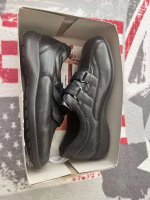 Svarta skinnsneakers från Waldläufer - Säljer ett par svarta sneakers från Waldläufer med två breda kardborreband över foten. Skorna har en rund tå och är tillverkade i mjukt skinn med diskreta sömmar och platt sula. Perfekt för dig som vill ha bekväma och stilrena skor.