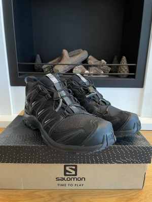 Svarta Salomon XA Pro 3D  - Salomon XA Pro 3D sneakers i helsvart med robust mesh och syntetmaterial. Skorna har snabbsnörning, grov sula för bra grepp och detaljerade loggor på sidan och plösen. 