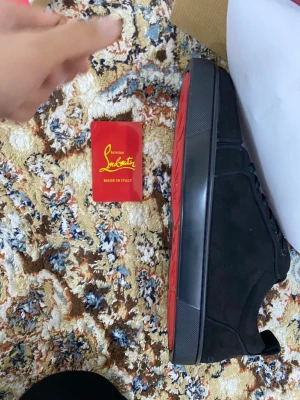 Christian Louboutin svarta sneakers - Säljer ett par svarta sneakers från Christian Louboutin med ikonisk röd sula och snygg snörning. Skorna är tillverkade i mocka och har en platt sula med rund tå. Kommer med originalkartong och tillbehör. Perfekt för dig som gillar exklusiva märken och stilren design.