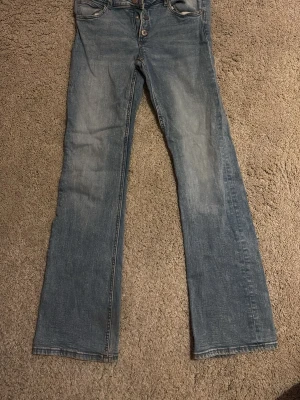 Blå bootcut jeans från Gina Tricot - Säljer ett par klassiska blå jeans från Gina Tricot med bootcut passform och låg midja. Jeansen har knäppning med tre knappar. 