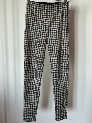 Brun och vita hundtands byxor - Leggings/ byxor med brunvity hundtandsmönster. De har hög midja och smal passform, med dragkedja i sidan för enkel påklädning. Polyester & elestan, 