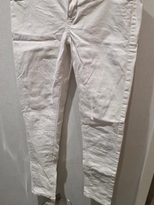 Vita skinny jeans från Jegging Jane - Säljer ett par vita skinny jeans från Jegging Jane i storlek M. Byxorna har klassisk femficksdesign, silverfärgad knapp med text och smal passform. Materialet är mjukt och stretchigt, perfekt för dig som gillar en tajt look.