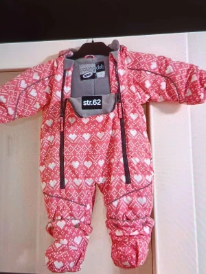 Rosa täckbyxdress med hjärtan Young Club - Säljer en gullig rosa täckbyxdress från Young Club med vitt hjärtmönster och praktiska dragkedjor framtill. Dressen har huva och är fodrad för extra värme, perfekt för kyliga dagar. Mjuk och bekväm passform för de minsta.