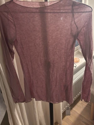 Ljuslila långärmad mesh-topp - Säljer en tunn och transparent ljuslila långärmad topp i meshmaterial. Perfekt att styla lager på lager eller bära som den är för en trendig look. Toppen har en rund halsringning och är figurnära i modellen.