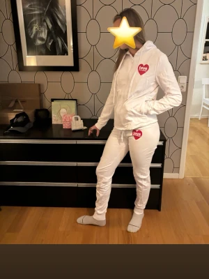 Exklusiv Moschino-mysdress i vit – knappt använd! - Exklusiv vit mysdress från Moschino, knappt använd och i perfekt skick. Lyxig design med mjukt material – perfekt för både hemmamys och stilfull lounge-look. Enda anmärkningen: etiketten i byxan har lossnat i ena kanten. Ett unikt plagg för den som vill kombinera komfort med mode.