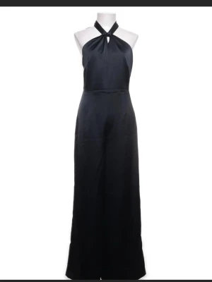 Svart byxdress med omlott och knyt - Snygg svart byxdress med omlott-hals och breda ben. Materialet är silke och knytning i nacken som ger en öppen rygg. Passformen är loose och stilen är wide, perfekt för dig som gillar en elegant look