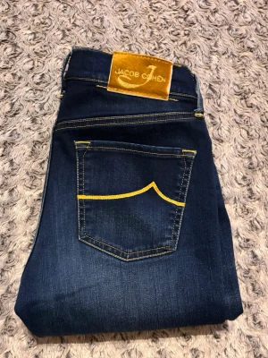 Jacob Cohen - Snygga mörkblå jeans från Jacob Cohen med skinny passform och kontrasterande gula sömmar. Klassisk femficksmodell med gul patch bak i midjan. Jeansen är tillverkade i stretchig denim för extra komfort och har en stilren look.