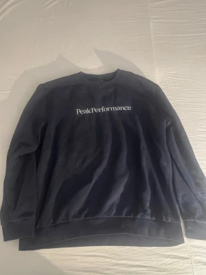 Mörkblå sweatshirt Peak Performance XL - Säljer en mörkblå sweatshirt från Peak Performance i storlek XL. Tröjan har klassisk rund halsringning, ribbade muddar och logga broderad i vitt framtill. Perfekt för dig som gillar enkel och stilren design.