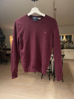 Vinröd merinoullströja Polo Ralph Lauren - Säljer en vinröd långärmad tröja från Polo Ralph Lauren i slim fit. Tröjan är gjord i tvättbar merinoull och har en klassisk rund halsringning samt den ikoniska broderade loggan på bröstet.