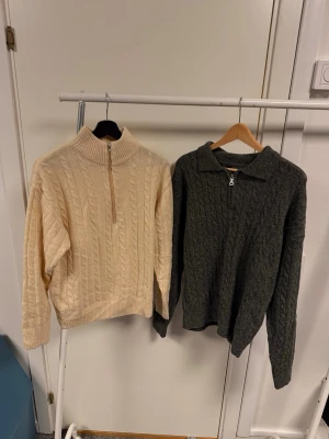 Stickad polotröja med half zip - Säljer två stickade polotröjor med half zip. Ena är beige och den andra mörkgrå, båda med klassiskt kabelstickat mönster. Perfekta för kyliga dagar och har lång ärm och ribbade muddar. Snygga att styla till jeans eller kjol.