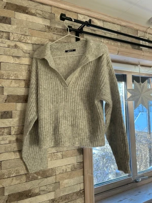 Ljusgrå stickad tröja Gina Tricot - Mysig ljusgrå stickad tröja från Gina Tricot med krage och v-ringad hals. Tröjan har ribbad struktur och långa ärmar, perfekt för kyliga dagar. Enkel att styla med både jeans och kjol.