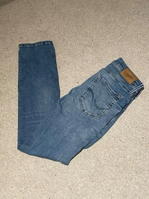 Blå jeans från Jack & Jones - Snygga blå jeans från Jack & Jones med klassisk femficksdesign och ljus tvätt. Jeansen har rak passform och normal midja, med tydliga sömmar och läderpatch bak i midjan. Materialet är slitstarkt denim i bomull. Perfekt för dig som gillar en enkel och stilren look.