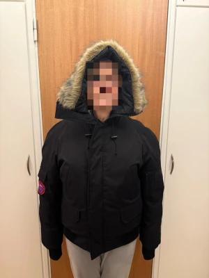 Herr first slope expedition jacka - Säljer en svart pufferjacka med stor huva och fuskpäls runt kanten. Jackan har flera fickor, ribbade muddar och patch på ärmen. Perfekt för kalla dagar och riktigt skön passform. Stängs med dragkedja och knappar framtill. Herr jacka strl S men kan funka på M.  (på bilden har en tjej på sig jackan)