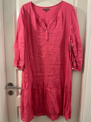 Rosa långklänning från Fiore - Säljer en rosa långklänning från Fiore i storlek L. Klänningen har trekvartsärm, v-ringad hals med knappdetalj och volang nedtill. Tillverkad i linne, vilket gör den skön och luftig. Perfekt för dig som gillar enkel och stilren design.