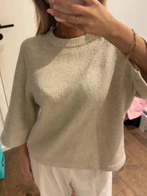 Beige stickad tröja med vida ärmar - Mysig beige stickad tröja med rund halsringning och vida trekvartsärmar. Tröjan har en avslappnad passform och ribbade detaljer vid halsen. Perfekt för lager på lager under kyligare dagar. Viral tröja från Nelly som går att styla på många sätt!