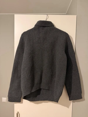 Mörkgrå polotröja Acne Studios ull - Säljer en mörkgrå, ribbstickad polotröja från Acne Studios i 100% ull. Tröjan har hög krage och lång ärm. Storlek L men mer som en M. Perfekt för kalla dagar och enkel att styla till jeans eller byxor.