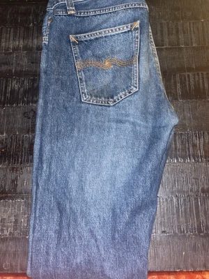 Blå jeans från Nudie Jeans - Säljer ett par snygga blå jeans från Nudie Jeans med snyggt mönster och en skön wash som börjar komma. Jeansen har normal passform och modellen Gritty Jackson, strl W28 & L32. Lite slitna längst ner i hälarna därav går de att få ganska billigt!