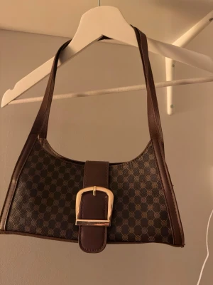 Brun axelväska med mönster och spänne - Snygg brun axelväska 