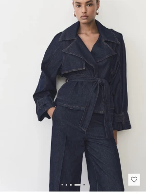 Mörkblå jeansjacka med bälte - Snygg mörkblå jeansjacka med bred krage och knytskärp i midjan. Jackan har långa ärmar med detaljer vid ärmslut och markerade sömmar som ger en cool look. Perfekt för dig som gillar en trendig och avslappnad stil. Har bara andvänts 1 gång 