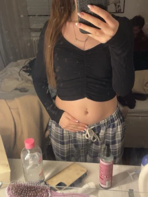 Svart croppad topp  - Säljer en svart långärmad croppad topp från NLY Trend i storlek XS. Toppen har v-ringning och snygg rynkdetalj med snörning framtill som ger en cool look. Perfekt att styla med jeans eller kjol för en trendig outfit.