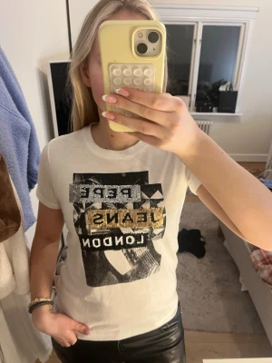 Vit t-shirt från Pepe Jeans med paljetter - Vit t-shirt från Pepe Jeans med coolt tryck och paljettdetaljer i silver, guld och svart. Kortärmad modell i mjuk bomull, med texten 'PEPE JEANS LONDON' och grafiskt motiv på framsidan. Perfekt för dig som gillar statement-plagg. St xs men passar S, !! KÖP GÄRNA VIA VINTED ISTÄLLET!!